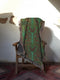 A woven cotton throw featuring an intricate luna moth design in deep green and russet tones, framed by soft fringe.